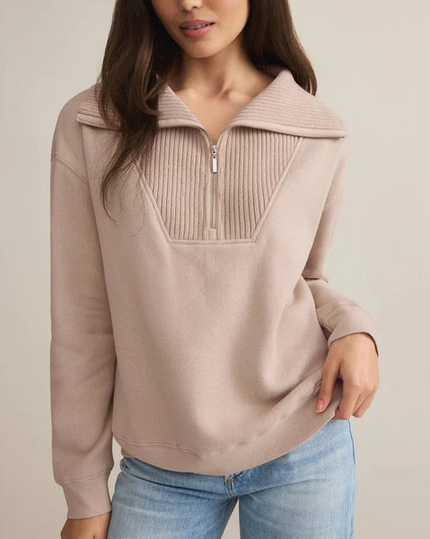 Woman wearing a beige pullover with a zipper and blue jeans on a plain background