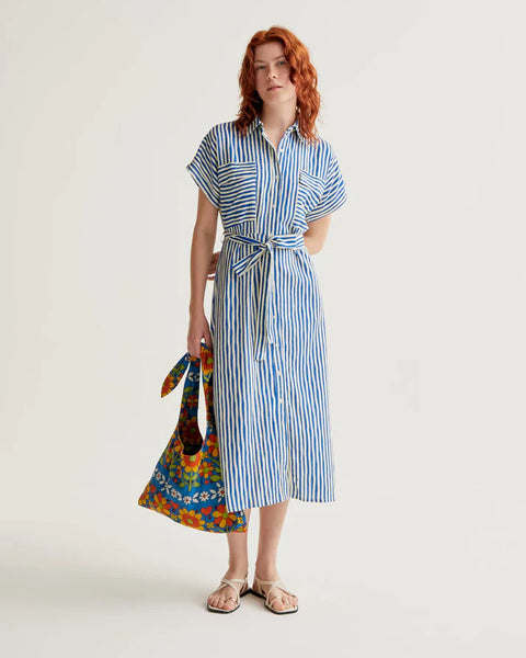 Woman wearing a blue and white striped dress holding a colorful bag on a plain background