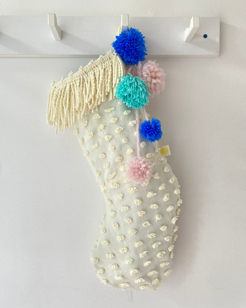 Decorative Christmas stocking with pom-poms hanging on a white wall.