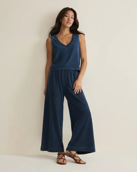 Woman wearing a blue sleeveless top and wide-leg pants against a beige background
